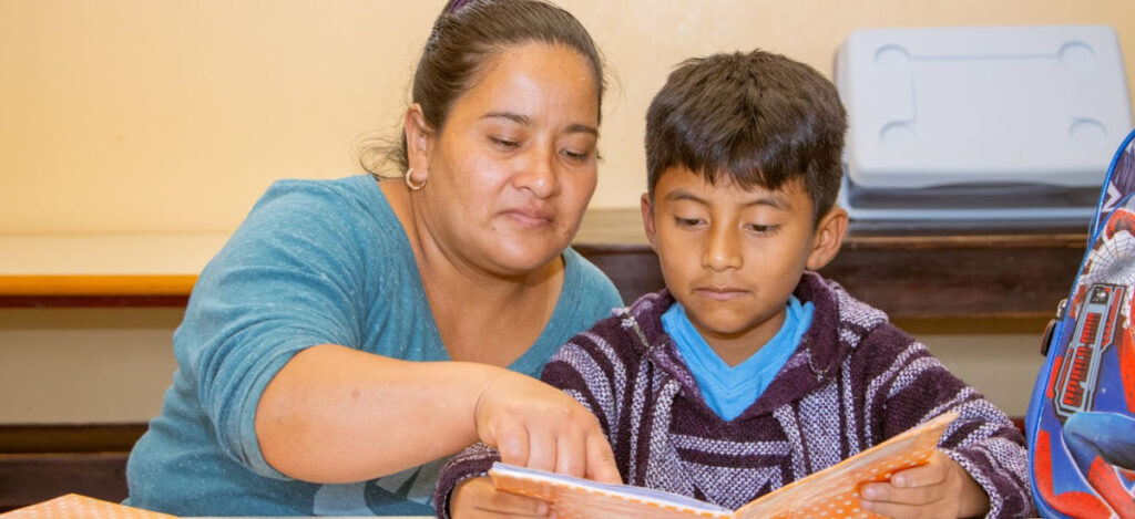 OlgawithSon_5318_WEB A guatemalan woman sitting beside a young boy and pointing at the words in a book he is reading