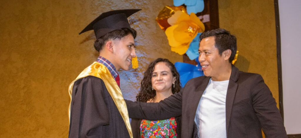 HectorandErickaatGrad_1469 Pastor Hector congratulating a student in graduation gown while Ericka looks on