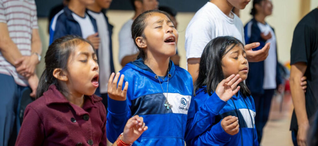 worship-WEB Three guatemalan girls with eyes closed and hands raised in worship