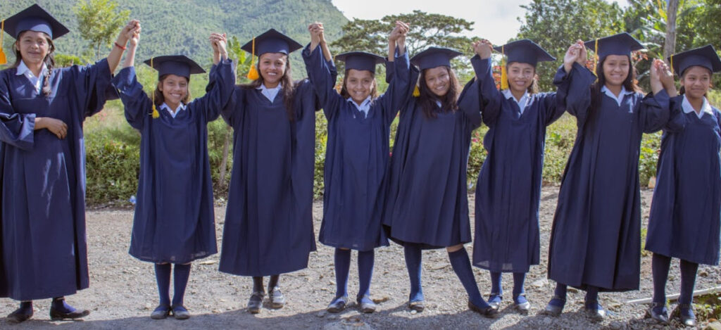 TogetherUntilGraduation_7055_WEB Guatemalan teens in black grad caps and gowns standing in a row with joined hands raised