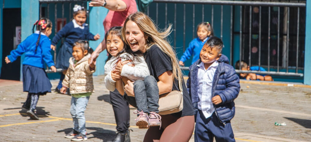 excitementofsponsorvisit_WEB A young Guatemalan girl with a big smile in the arms of a North American woman with an equally big smile running in the midst of a group of kids playing some sort of game